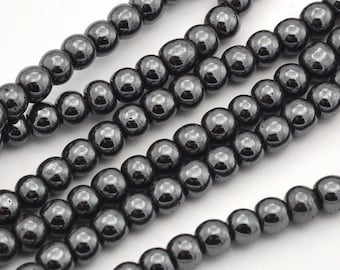 May include: A strand of black hematite beads, each bead is round and smooth. The beads are strung on a clear thread and are arranged in a loose, flowing pattern.