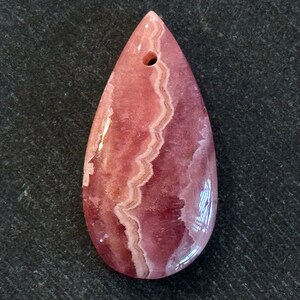 May include: A pink and white teardrop-shaped pendant made of polished gemstone with a hole at the top for stringing.
