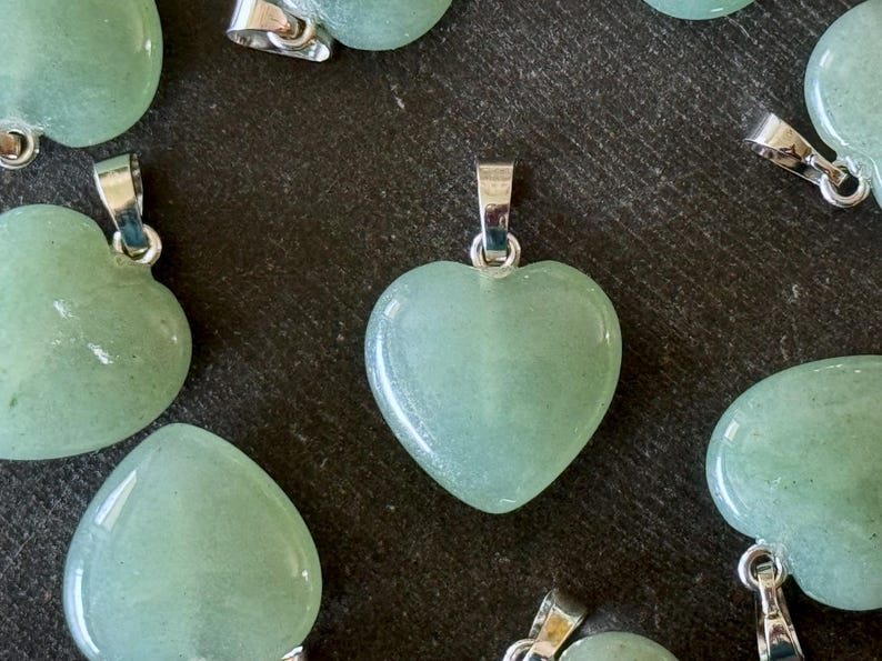 May include: A collection of green heart-shaped pendants with silver bail. The pendants are made of polished stone and have a smooth, glossy finish.