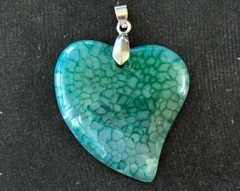 Puede incluir: Un colgante en forma de corazón hecho de ágata verde con una argolla de plata. El ágata tiene un patrón único y arremolinado.