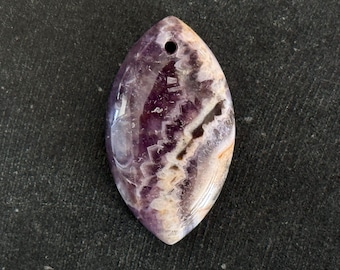 May include: A marquise-shaped amethyst pendant featuring deep purple and white banded patterns with a smooth, polished finish. The stone has a small circular hole drilled near the top point for suspension, showcasing natural mineral variations.