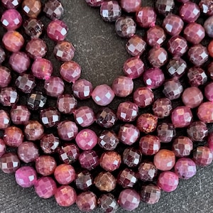 May include: A strand of faceted ruby beads, with a deep red color and a slightly irregular shape. The beads are strung on a clear thread and are ready for jewelry making.