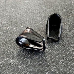 May include: Two black metal thimble-shaped objects are displayed on a gray surface. The objects have a shiny, reflective surface and a curved design. One is positioned on its side, while the other stands upright.