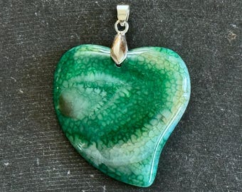 Puede incluir: Colgante de corazón de ágata verde y blanca con una anilla de plata. La ágata tiene un patrón de remolino de verde y blanco.