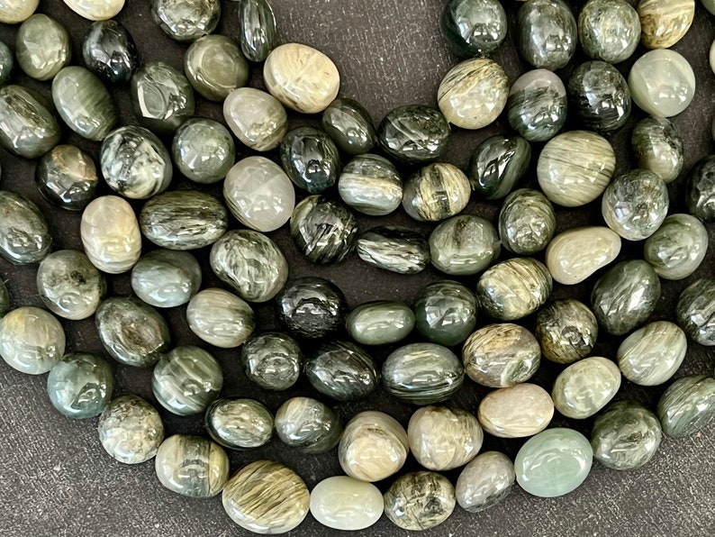 Pode incluir: Uma cole&ccedil;&atilde;o de pedras roladas em tons de verde, cinza e branco. As pedras t&ecirc;m uma apar&ecirc;ncia lisa e polida e padr&otilde;es variados, criando uma est&eacute;tica natural e org&acirc;nica. Ideal para fazer joias ou para fins decorativos.