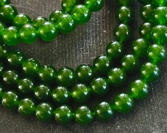 Op de afbeelding: Een streng groene jade kralen, elke kraal is rond en glad. De kralen zijn aan elkaar geregen op een doorzichtig draad. De kralen zijn in een losse stapel gelegd, met enkele kralen die overlappen.
