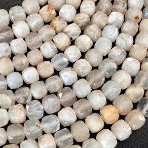 May include: Close-up of a strand of faceted, off-white gemstone beads. The beads have a subtle, translucent quality with variations in color, ranging from clear to pale yellow and gray. The beads are evenly sized and shaped.