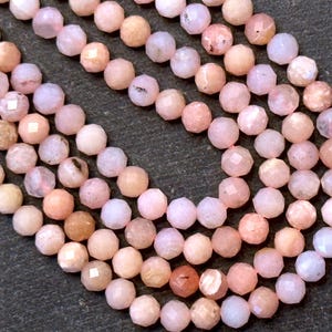 May include: Close-up of strands of faceted, round gemstones in shades of pink, peach, and cream. The beads have a subtle sparkle and are strung together, creating a delicate and elegant appearance. The gemstones are likely used for jewelry making.