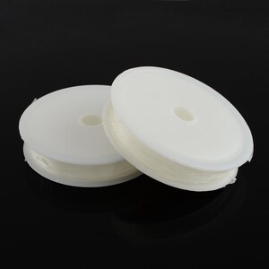 May include: Two spools of clear, elastic beading cord. The cord is wound around white plastic spools. The background is a solid black.