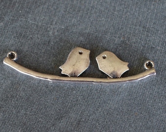 Pode incluir: Encanto de prata com dois pássaros empoleirados em um galho com laços em cada extremidade para prender a um colar ou pulseira.