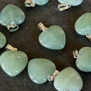 May include: A collection of eight green heart-shaped pendants with silver bail attachments. The pendants are made of polished stone and have a smooth, glossy finish.