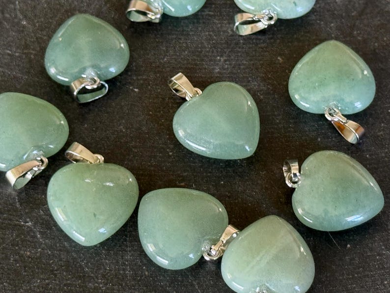 May include: A collection of eight green heart-shaped pendants with silver bail attachments. The pendants are made of polished stone and have a smooth, glossy finish.