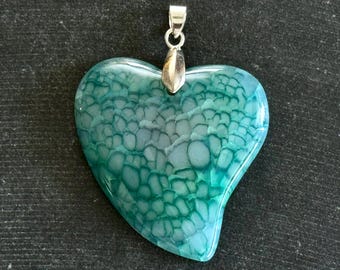 Puede incluir: Colgante en forma de corazón con una fianza plateada. El colgante es una mezcla de verde azulado y turquesa, con un patrón texturizado único. La piedra preciosa está pulida y tiene un acabado brillante. Una hermosa joya.