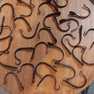 May include: A collection of black metal hooks, all in the shape of a simple 'S' curve, are scattered on a wooden surface. The hooks are all different sizes and shapes, but they are all made of the same metal.