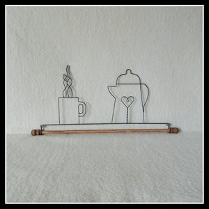 May include: A wire art piece depicting a coffee cup with steam, a teapot with a heart, and a wooden rod. The black wire art is mounted on a shelf with wooden dowel ends. The background is a light, textured surface.