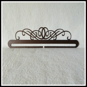 May include: A brown metal medal display rack with a decorative scroll design. The rack has two rows of hooks for hanging medals.