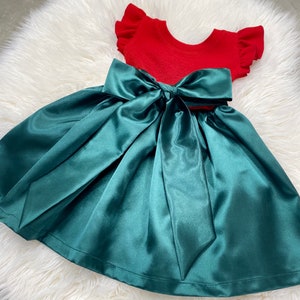 Op de afbeelding: Een groene satijnen rok met een grote rode strik. De rok is perfect voor een feestje tijdens de feestdagen of een speciale gelegenheid.