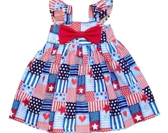 May include: A red, white, and blue patchwork dress with a red bow. The dress has a ruffled neckline and straps. The fabric is a cotton blend.