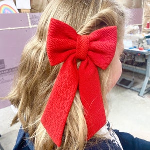 Op de afbeelding: Een felrode strik van textuurstof. De strik is in een simpele knoop geknoopt en heeft lange linten die naar achteren hangen.