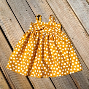May include: A yellow dress with white polka dots and a bow at the neckline.
