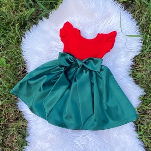 Op de afbeelding: Een groene satijnen jurk met een rood lijfje en een grote groene satijnen strik in de taille.