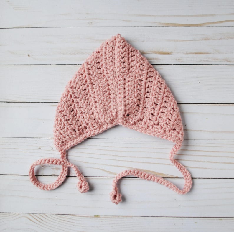 Pu&ograve; includere: Un berretto per neonato in crochet rosa con lacci. Il berretto &egrave; realizzato con un semplice motivo a punto e ha una forma a punta.
