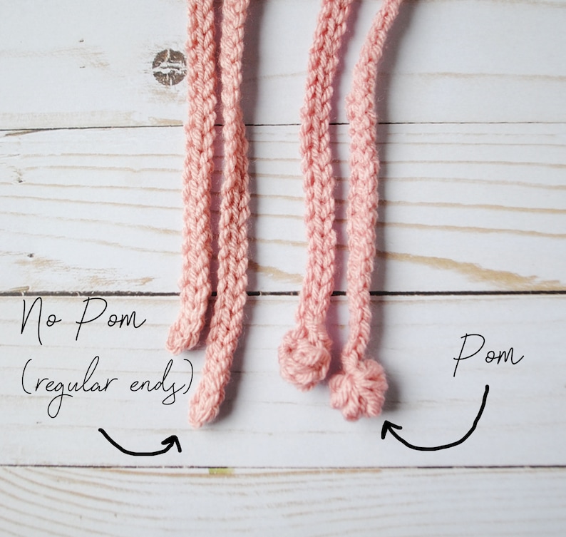 Pu&ograve; includere: Due cordoni di uncinetto rosa, uno con un'estremit&agrave; normale e l'altro con un'estremit&agrave; a pompon. Il testo "No Pom (regular end)" &egrave; scritto accanto al cordone con un'estremit&agrave; normale, e il testo "Pom" &egrave; scritto accanto al cordone con un'estremit&agrave; a pompon.