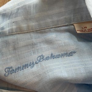Puede incluir: Camisa de lino azul claro con el logo "Tommy Bahama" bordado. La camisa es talla L/G y est&aacute; hecha en China. La tela tiene un patr&oacute;n sutil.