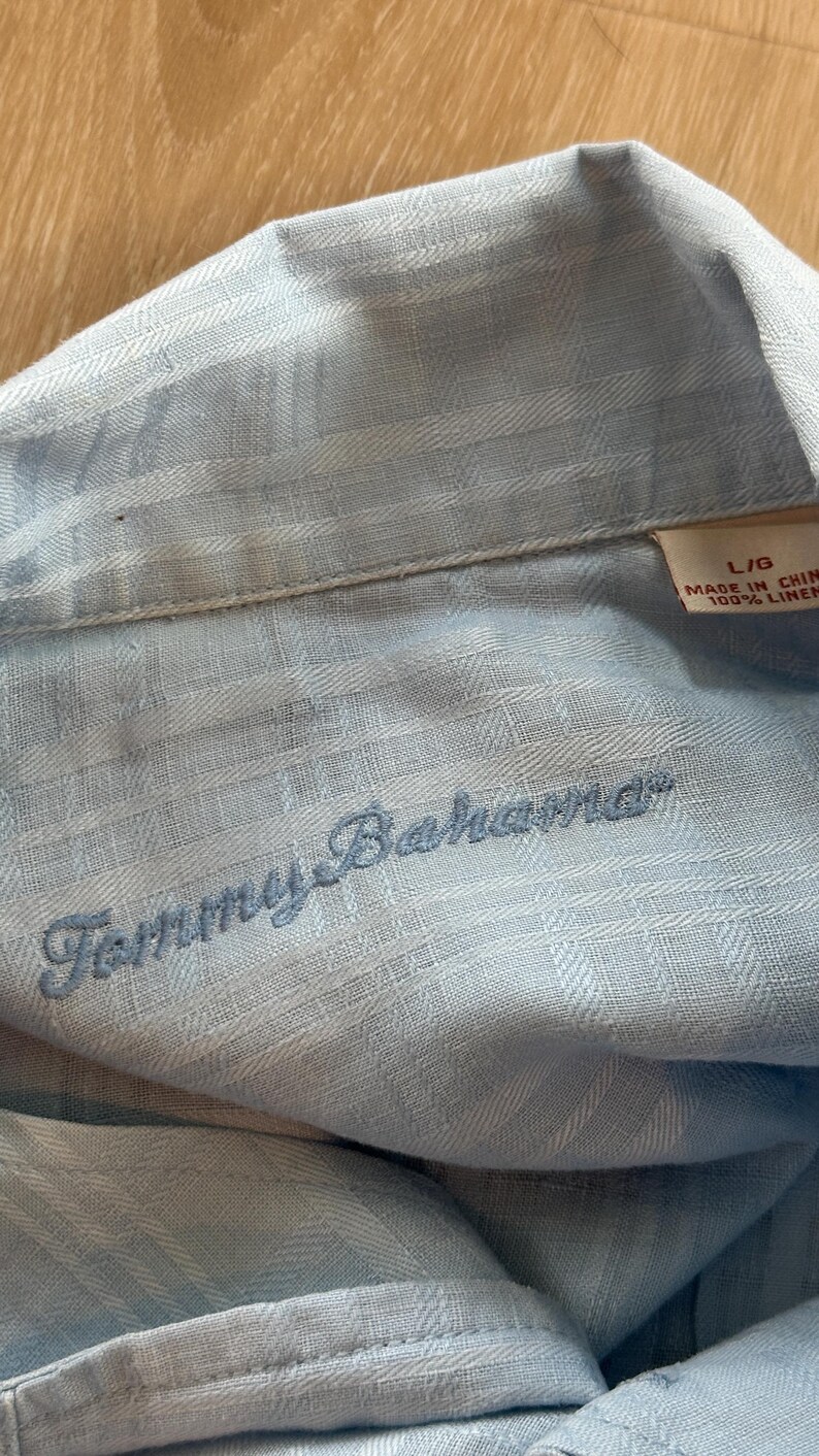 Puede incluir: Camisa de lino azul claro con el logo "Tommy Bahama" bordado. La camisa es talla L/G y est&aacute; hecha en China. La tela tiene un patr&oacute;n sutil.