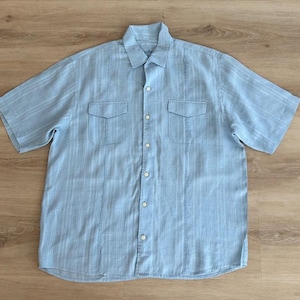 Puede incluir: Camisa azul claro de manga corta con estampado de rayas verticales. La camisa tiene dos bolsillos en el pecho y una botonadura frontal. El cuello es un cuello cl&aacute;sico. La camisa est&aacute; hecha de tela ligera.