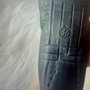 Puede incluir: Una suela de zapato negra con una superficie texturizada con ranuras verticales y un emblema circular que contiene el n&uacute;mero 36. El texto P/650 est&aacute; grabado cerca del borde superior de la suela, que muestra signos de desgaste y pliegues visibles.