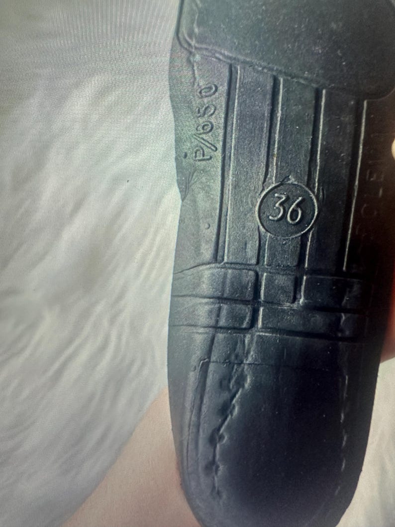 Puede incluir: Una suela de zapato negra con una superficie texturizada con ranuras verticales y un emblema circular que contiene el n&uacute;mero 36. El texto P/650 est&aacute; grabado cerca del borde superior de la suela, que muestra signos de desgaste y pliegues visibles.