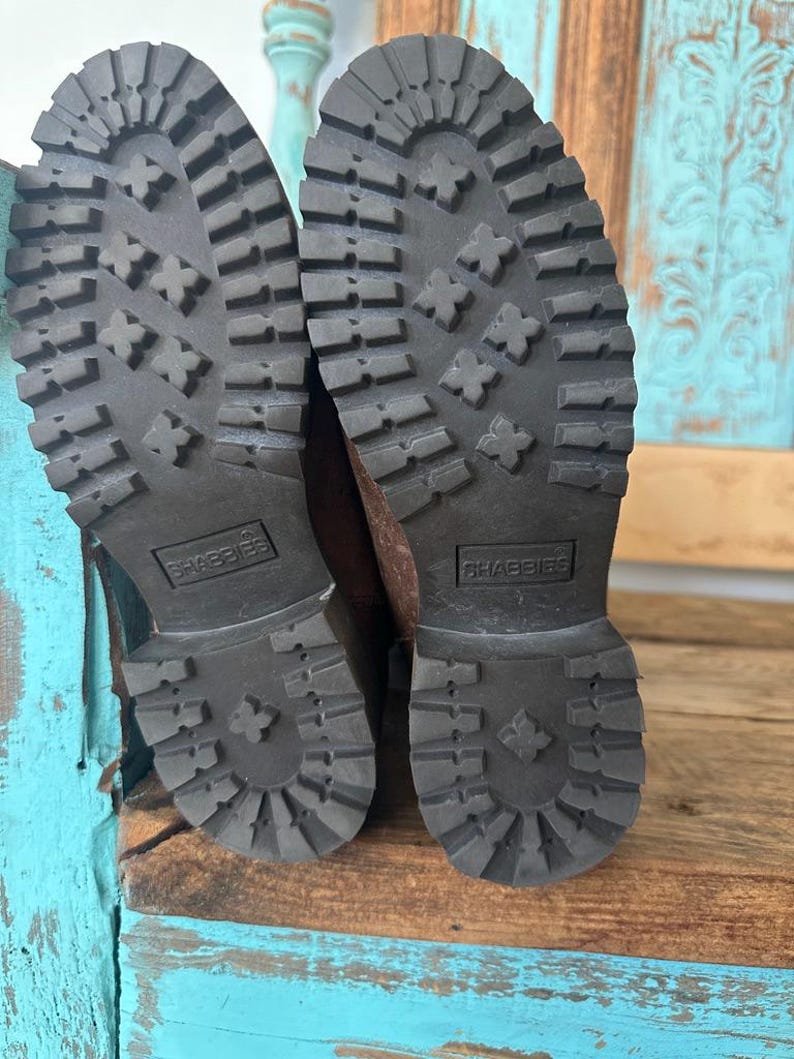 Puede incluir: Un par de botas de color marr&oacute;n oscuro con suelas de goma negra gruesas y tacos profundos para mayor tracci&oacute;n. Las suelas tienen un tac&oacute;n prominente y un patr&oacute;n texturizado, con la marca SHABBIES grabada en un recuadro rectangular.