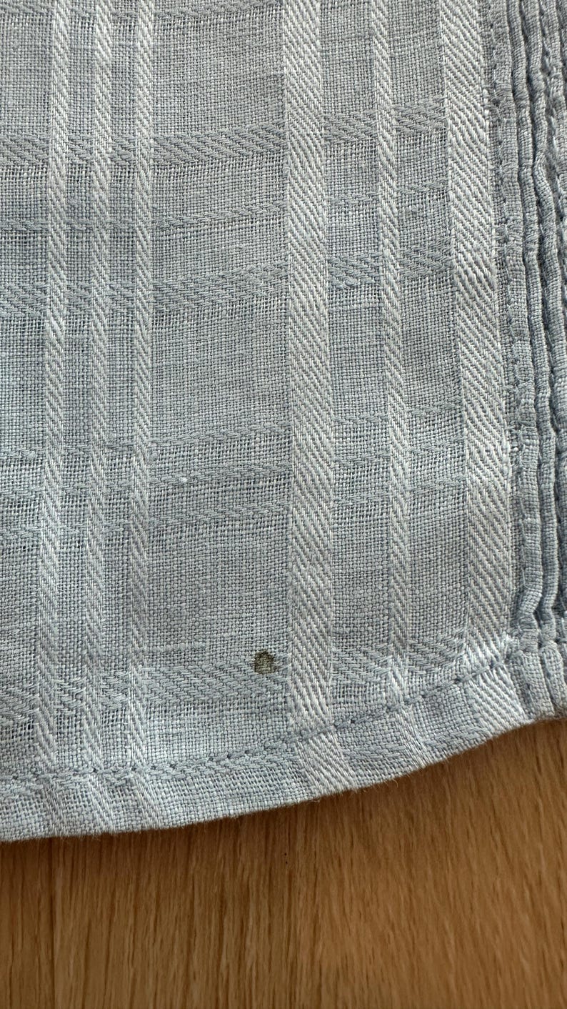 Puede incluir: Primer plano de una tela azul claro con un patr&oacute;n de rayas texturizado. La tela tiene una apariencia tejida con l&iacute;neas verticales y horizontales que crean un dise&ntilde;o similar a una cuadr&iacute;cula. El borde de la tela es visible, mostrando un dobladillo cosido.