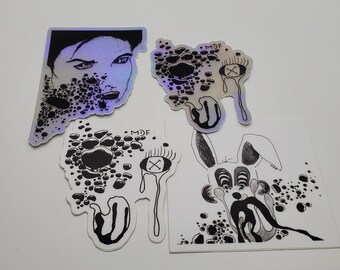 May include: Four black and white holographic stickers with abstract designs. The stickers feature a face, an eye, a dripping eye, and a rabbit with a dripping mouth. The stickers have a black and white design with a holographic finish.