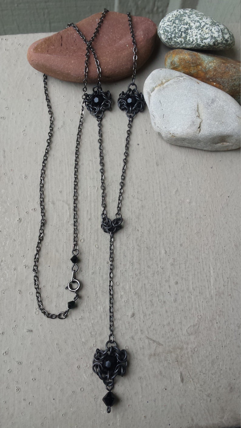May include: A black chain necklace with three black crystal accents. The necklace is made of metal and has a delicate, intricate design.