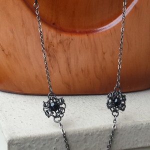 May include: A black chain necklace with three black gemstone accents in a delicate, intricate design. The necklace is displayed on a wooden mannequin.