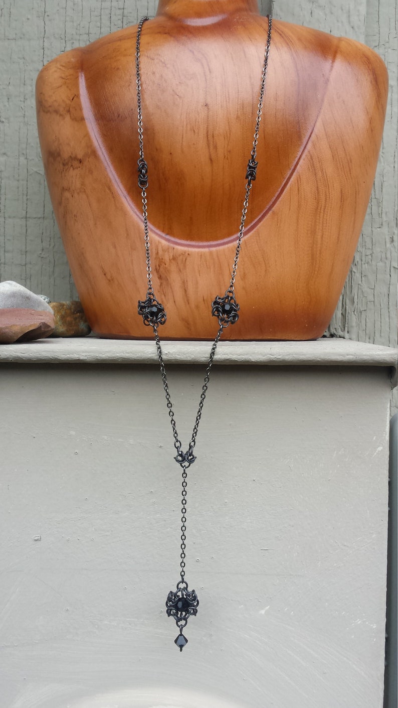 May include: A black chain necklace with black bead accents and a black pendant. The pendant is a detailed design with a black bead in the center.