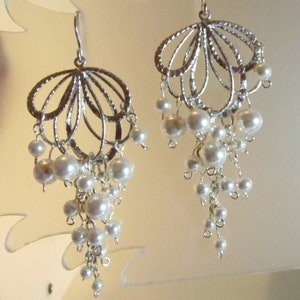May include: Silver dangle earrings with a delicate, openwork design and a cluster of white pearls hanging from each earring.