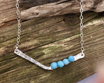 May include: A silver necklace with a hammered bar pendant and four light blue gemstone beads.
