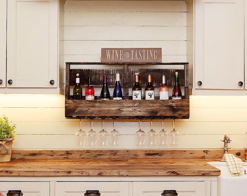 May include: A dark brown wooden wall-mounted wine rack featuring a horizontal shelf for eight wine bottles and a lower rack for hanging eight wine glasses. A rectangular sign with the text WINE TASTING is positioned on top of the wooden rack.
