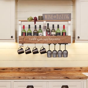 May include: A wall-mounted wooden wine rack with a white frame and natural wood shelf. The front panel features the text "Create your own Happiness" and the top shelf displays a "WINE TASTING" sign, wine bottles, and mugs and glasses hanging below.