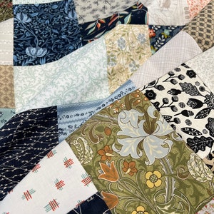 May include: Close-up of a patchwork quilt with various fabric patterns. The quilt features a mix of floral, geometric, and abstract designs in shades of blue, green, brown, and white. The fabrics are arranged in a geometric pattern.
