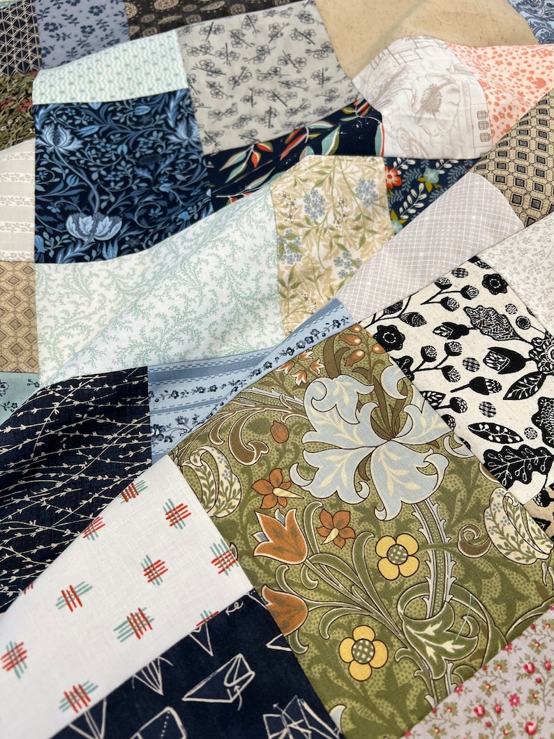 May include: Close-up of a patchwork quilt with various fabric patterns. The quilt features a mix of floral, geometric, and abstract designs in shades of blue, green, brown, and white. The fabrics are arranged in a geometric pattern.