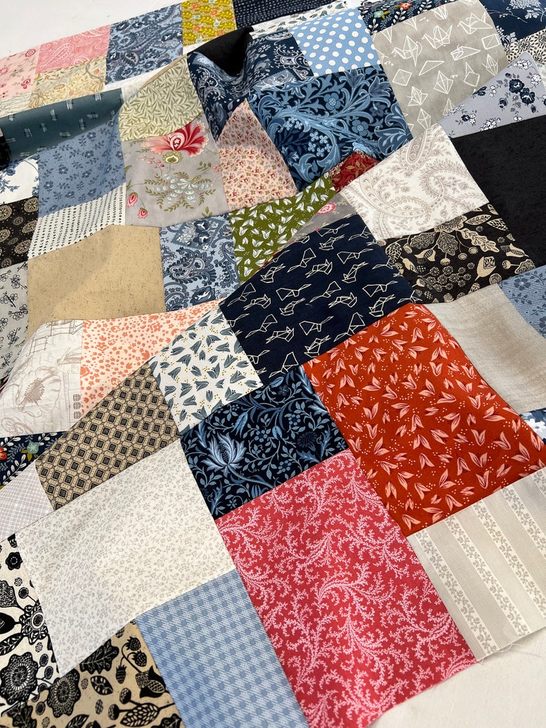 May include: A patchwork quilt featuring a mix of patterned fabrics in blue, red, beige, and black. The quilt showcases floral, geometric, and abstract designs, creating a visually diverse and textured surface. The quilt is made of multiple fabric squares.