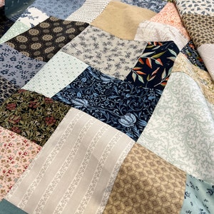 May include: A patchwork quilt featuring a mix of patterned fabrics in blue, beige, pink, and green. The quilt showcases floral, geometric, and striped patterns, creating a visually interesting textile.