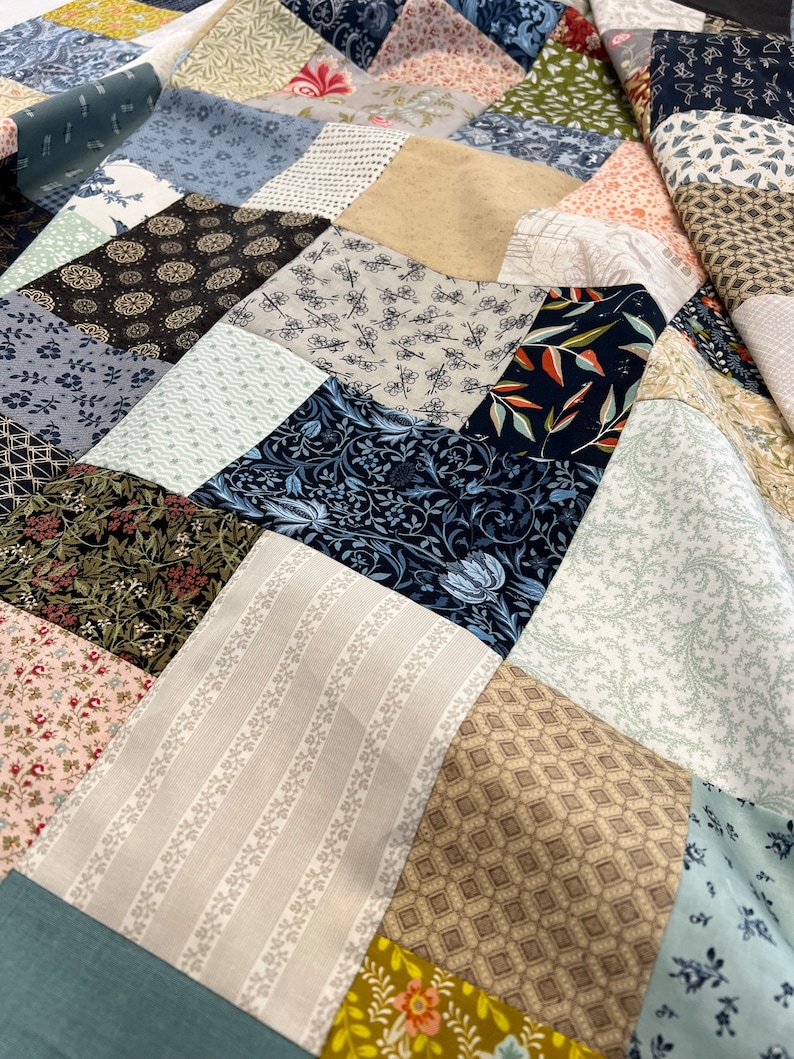 May include: A patchwork quilt featuring a mix of patterned fabrics in blue, beige, pink, and green. The quilt showcases floral, geometric, and striped patterns, creating a visually interesting textile.