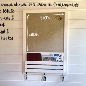 May include: White wall mounted message board with a cork surface and a shelf below. The board measures 23.6 inches by 25.6 inches. The shelf has two hooks on either side. The board has the text "LEON" on a card in the shelf.