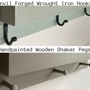 May include: A wooden shelf with the text "Anvil Forged Wrought Iron Hooks" and "Handpainted Wooden Shaker Pegs" on it. The shelf has three black metal hooks and two wooden pegs.