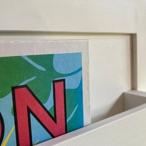 May include: Close-up of a colorful print with the letter "N" in red with a black outline. The print is partially inserted into a white shelf.